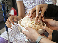 Une personne tient dans sa main un cerveau en plastique. Plusieurs mains touchent la texture.