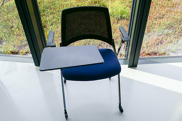Chaise avec pieds à roulettes et tablette intégrée sur la gauche de l’image, prise de vue légèrement en hauteur