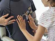 Les mains d'une jeune fille touchent un capteur brodé sur un t-shirt qui est présenté sur un buste.