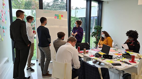 Un groupe de travail dans la salle C, certains sont assis autour d'une table, d'autre sont debout devant un tableau blanc